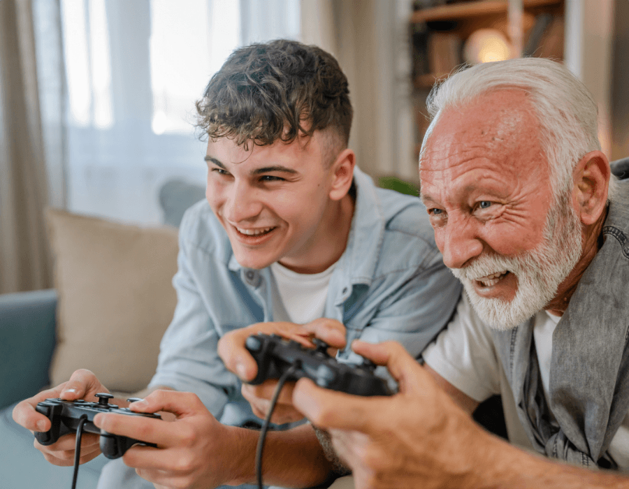 Enkel und Opa sitzen auf dem Sofa und zocken mit der Spielkonsole.