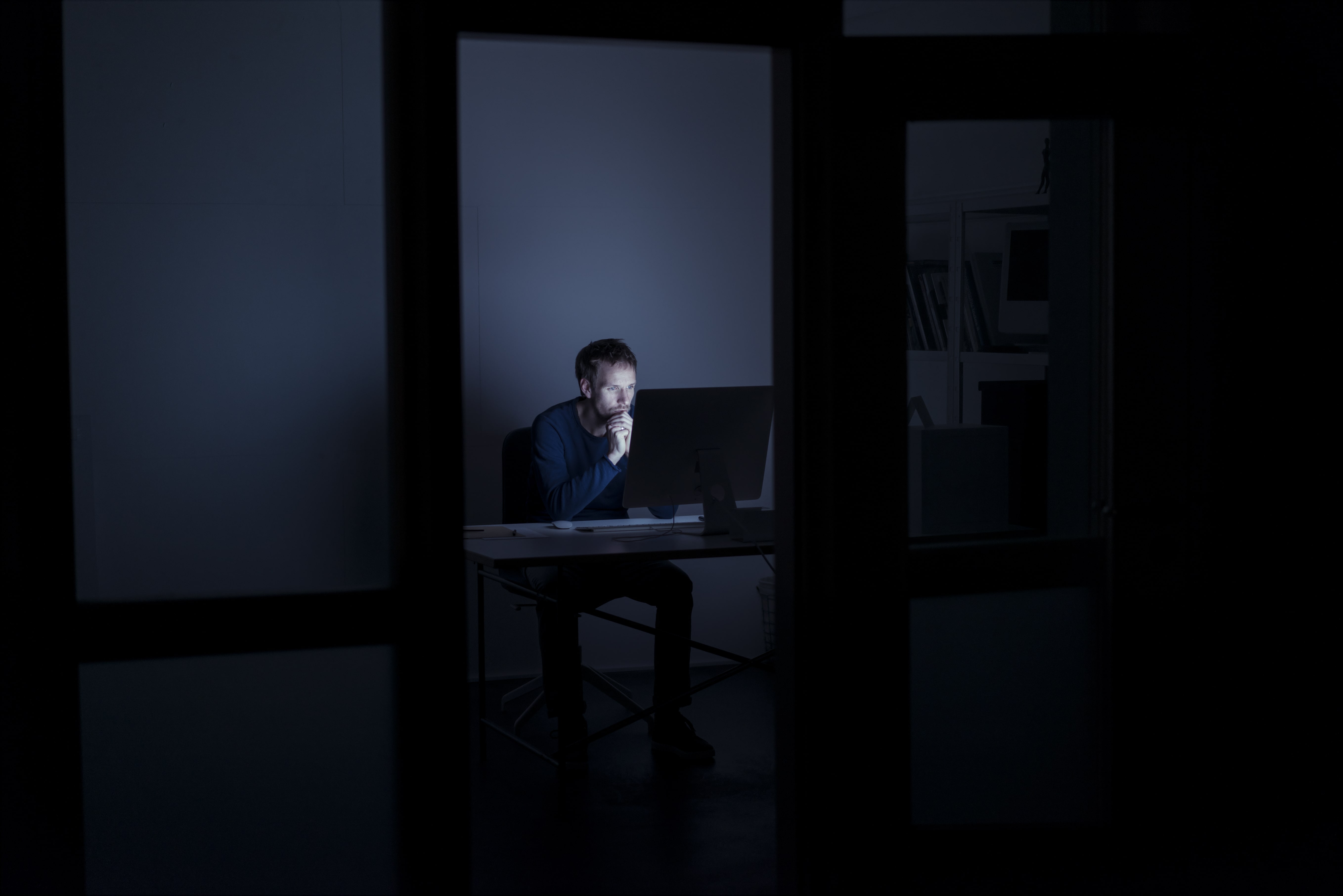 Ein Mann sitzt vor einem Rechner im Home-Office, im Zimmer gibt es bis auf den Bildschirm keine Lichtquelle.