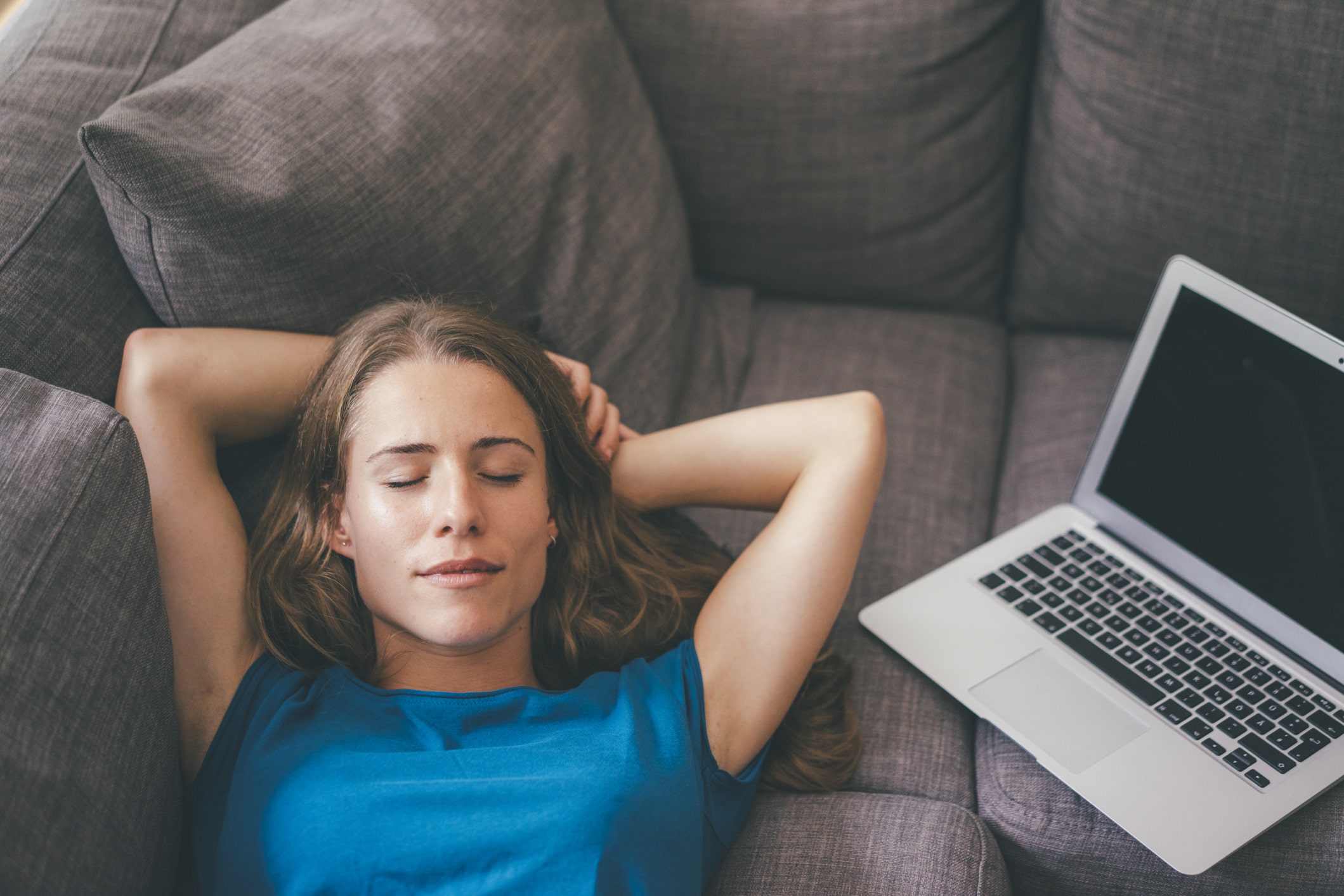 Eine Frau liegt auf dem Sofa, neben ihr ein Laptop, ihre Augen sind geschlossen.