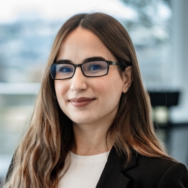  Portraitfoto von Hatice Erkekoğulları, Leiterin HR bei LWLcom. Sie hat lange braune Haare, trägt einen weißen Pullover und einen schwarzen Blazer, vor unscharfem Hintergrund.