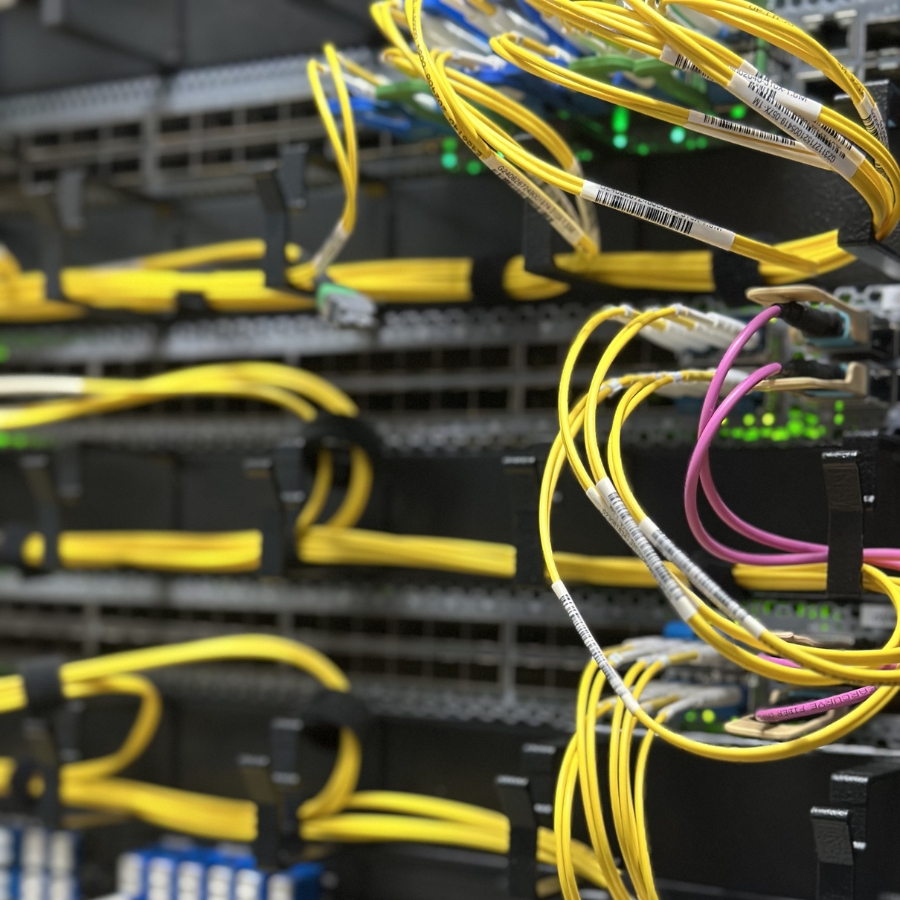 Verkabelter Server in einem Rack mit zahlreichen gelben und einigen violetten Netzwerkkabeln, grüne Status-LEDs sichtbar.